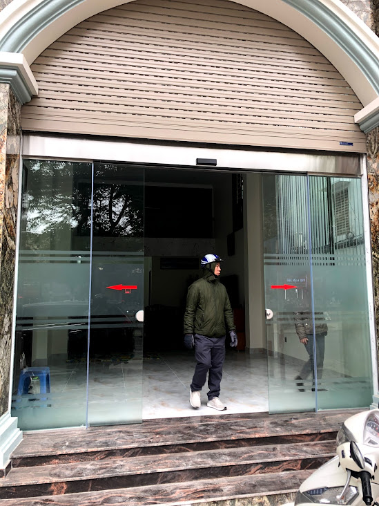 Cửa kính trượt tự động mặt tiền tòa nhà với người đàn ông đội mũ bảo hiểm đứng phía trong